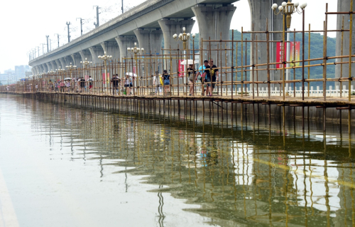 7月12日，行人從武漢湯遜湖橋上的臨時棧橋上走過。受暴雨影響，全長1000多米的武漢湯遜湖橋被猛漲的湖水中斷了橋面交通，至12日積水尚未退去。自7月8日起，為了方便群眾出行，江夏區在湯遜湖橋上開始施工搭建人行棧橋，目前行人可從已經搭建成功的棧橋上步行通過。新華社記者 程敏 攝