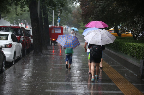 7月20日，行人在北京宣武門西大街上冒雨前行。