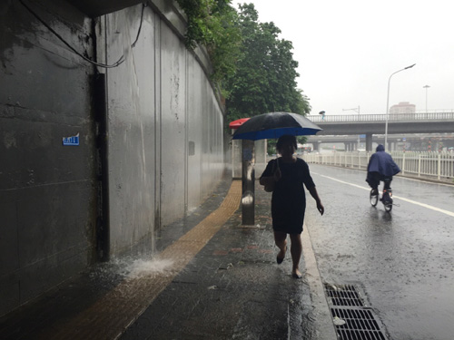 7月20日，行人走過北京蓮花橋橋下的一處排水口，隨著雨量增大此處排水口已經像個“小瀑布”。