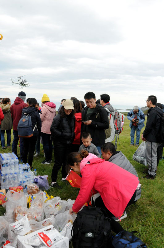  11月14日，在新西蘭凱伊庫拉小鎮，地震受困游客領取總領事館空運來的食品和瓶裝水，等待直升機分批救援。
