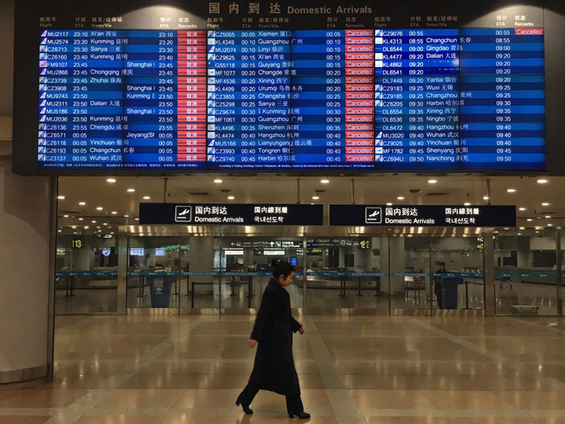 12月20日，在北京首都國際機場T2航站樓，一名工作人員走過顯示航班取消的電子屏幕。