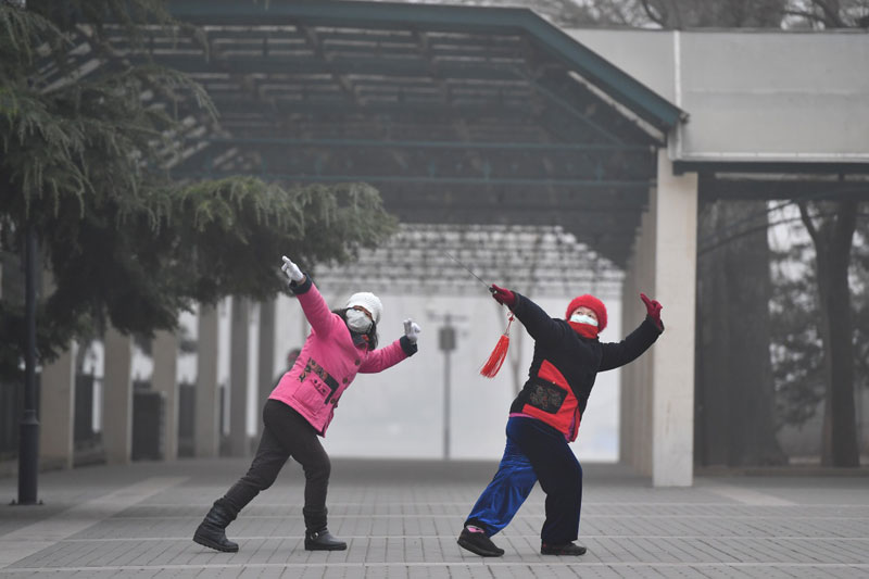 12月21日，兩名市民在霧霾籠罩的陶然亭公園內舞劍晨練。